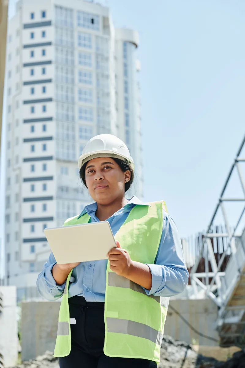 Person mit Schutzhelm und Tablet auf einer Baustelle